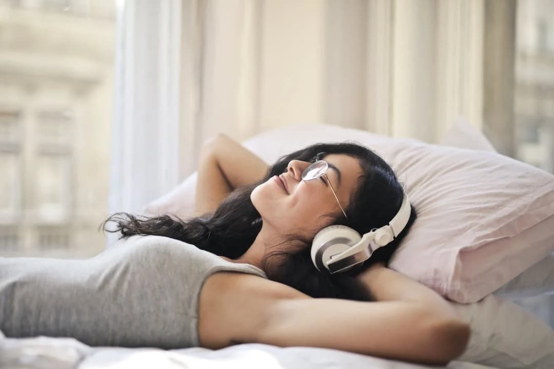 A woman is laying on the bed and listening to music